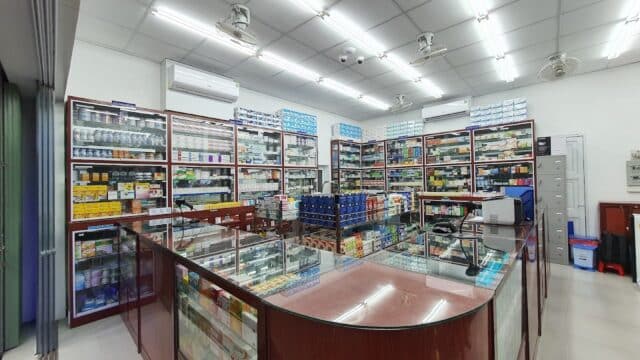 A well-lit Hoi An pharmacy with glass display counters and shelves filled with medicines and health products.