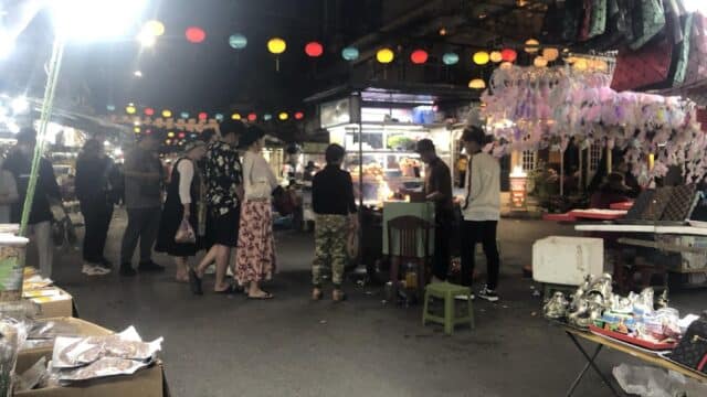 People browsing stalls at a lively Hoi An night market with colorful lanterns hanging overhead.