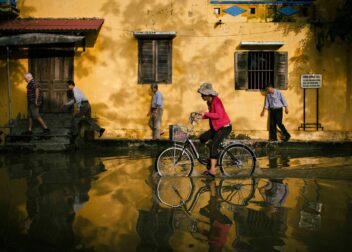 A cyclist rides through a flooded street in Hoi An, the water reflecting the old buildings