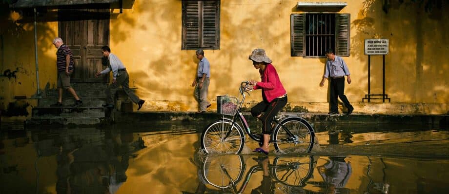 A cyclist rides through a flooded street in Hoi An, the water reflecting the old buildings