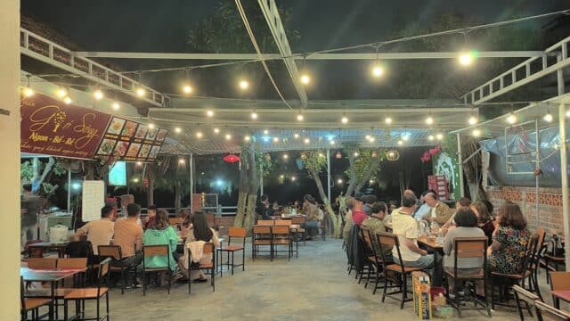 Outdoor Hoi An restaurant at night with string lights, lively diners, and trees in the background create a relaxed, vibrant atmosphere.