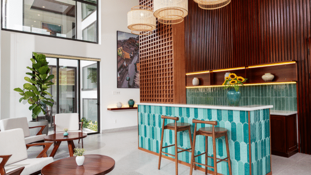Modern lounge with Hoi An-inspired teal-tiled bar, wood accents, wicker lights, sunflowers in a vase, and white chairs with round tables.