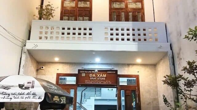 Two people dine at a small outdoor table in front of a three-story Hoi An building with balconies and plants.