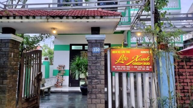 A guesthouse in Hoi An with green trim, gate, and a sign reading Lộc Xanh Green Bud at the entrance.