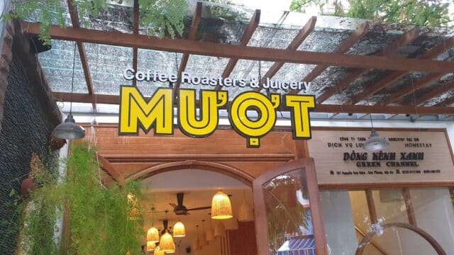 Entrance of MUỘT Coffee Roasters & Juicery in Hoi An, with yellow signage and hanging plants above.