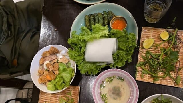 A table set with Hoi An Vietnamese dishes, fresh greens, grilled skewers, dipping sauces, and drinks.