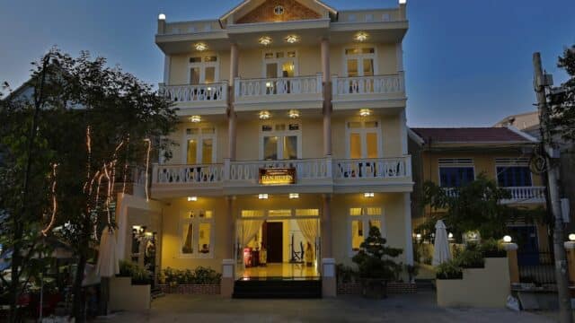 Three-story boutique hotel with lit windows and balconies in Hoi An, beautifully photographed at dusk from the street.