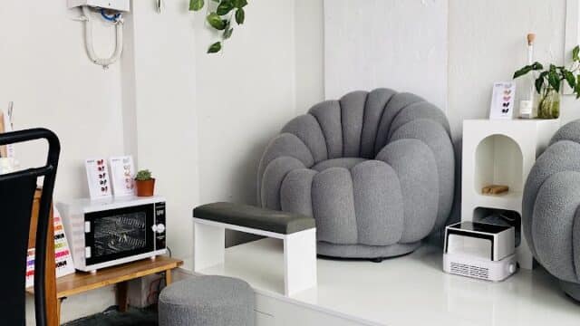 Modern, cozy salon in Hoi An with gray chairs, hanging plants, a small table, and minimal white decor on a concrete floor.