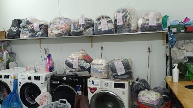 Laundry baskets and washing machines in a Hoi An laundromat, with bags of clothes labeled and stacked on shelves above.