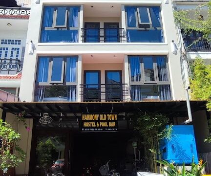 A three-story building with glass balconies in Hoi An, labeled Harmony Old Town Hostel & Pool Bar above the entrance.