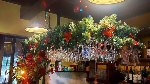 A bartender stands behind a festive Hoi An bar decorated with Christmas greenery, lights, and hanging wine glasses.