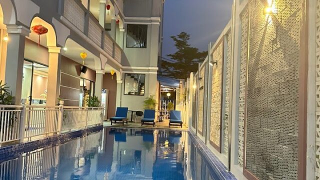Long, narrow pool beside a modern three-story building in Hoi An at dusk, with blue water and lounge chairs at the far end.