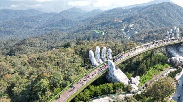 Golden Bridge near Hoi An, Vietnam, held by giant stone hands, with people walking and mountains in the background.