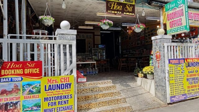 Entrance of a travel booking office in Hoi An with signs for laundry, motorbike rentals, and a souvenir shop in Vietnam.