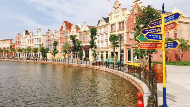 Colorful European-style buildings line a waterfront in Hoi An, with a multi-directional signpost in the foreground.