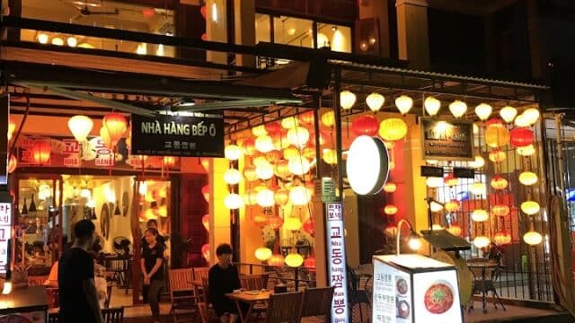 A brightly lit Hoi An restaurant with red and yellow lanterns outside, outdoor tables, and people sitting and walking at night.