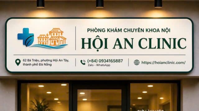 Hoi An Clinic entrance sign displays contact info, hours, and icons; Hoi An plants seen inside through the glass door.
