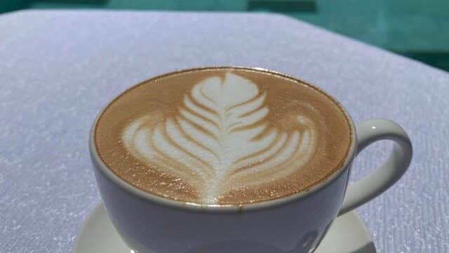 A cup of latte with leaf art sits on a white table by a pool in Hoi An, with a pink inflatable float in the background.