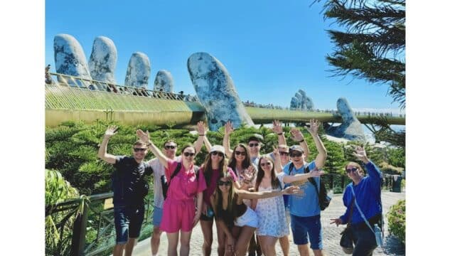 A group of friends smiles and poses in front of the Golden Bridge with giant hand sculptures near Da Nang and Hoi An, Vietnam.