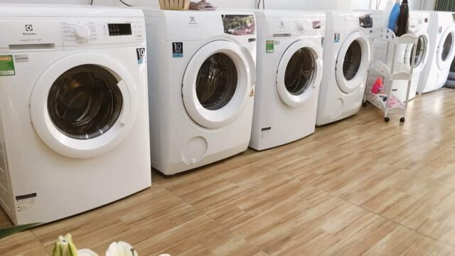A row of white washing machines in a clean Hoi An laundry room with wooden flooring and flowers in the foreground.