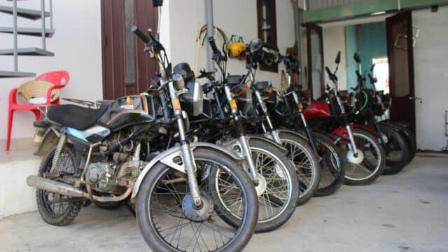 Several motorcycles are parked in a row inside a Hoi An garage, with a red plastic chair on the left side.