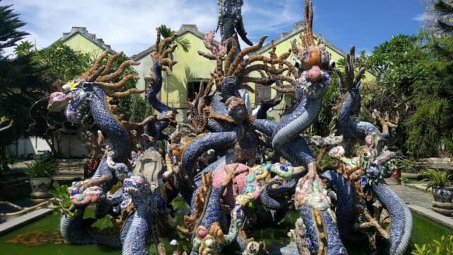 Colorful ceramic dragon sculptures rise from a pond in Hoi An, set against lush greenery and traditional buildings.