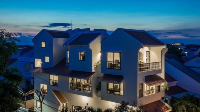 Modern white house with multiple balconies and large windows, illuminated at dusk against a blue Hoi An sky.
