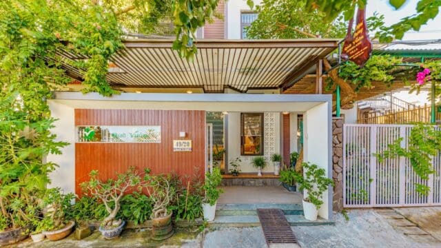 Modern house with a wooden facade, lush green plants, and metal roof—evoking the charming style of Hoi An on a sunny day.