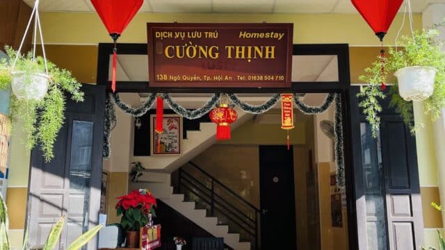 Homestay entrance in Hoi An with yellow walls, potted plants, and festive red lanterns and decorations.
