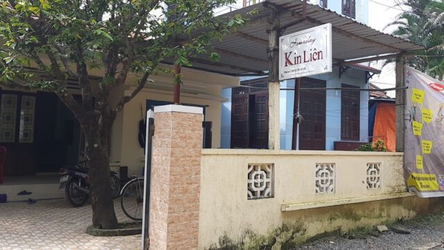 A guesthouse named Kim Liên in Hoi An with a sign, tree, bike, and yellow wall outside a building.