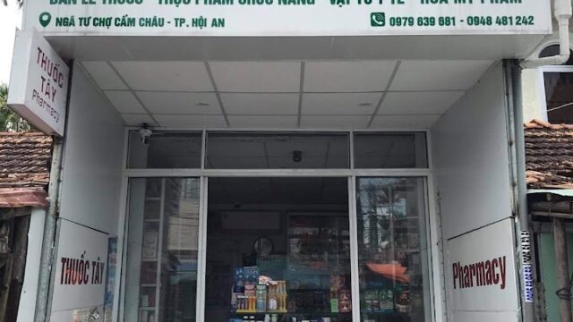 A pharmacy storefront in Hoi An with Vietnamese signs, a glass door, and various products displayed inside.
