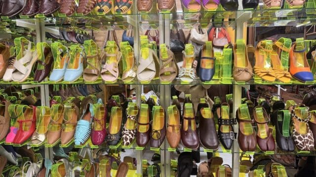 A display of colorful women's shoes, inspired by Hoi An, arranged neatly on glass shelves in a store.