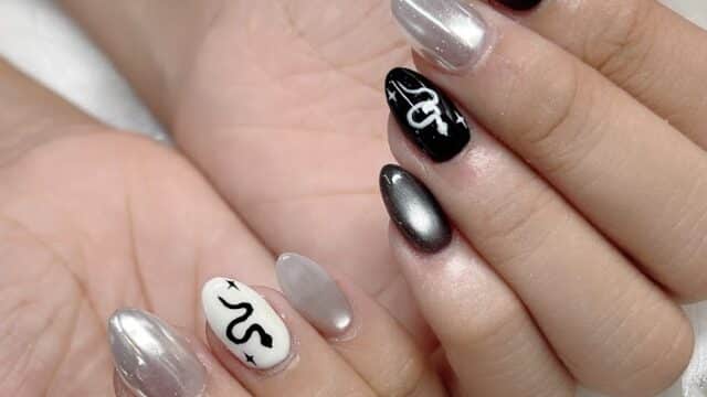 Hands with almond-shaped nails, featuring black, white, and silver polish inspired by Hoi An, some with snake designs and star accents.
