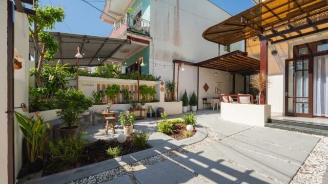 Sunny courtyard with potted plants, a small table with chairs, and modern buildings evoke a Hoi An-inspired landscaped garden.