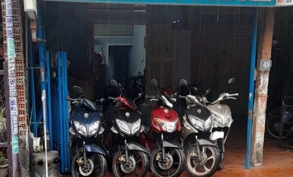 Four motorbikes are parked in front of a small Hoi An tour booking office with a blue and pink TOURPAL sign overhead.