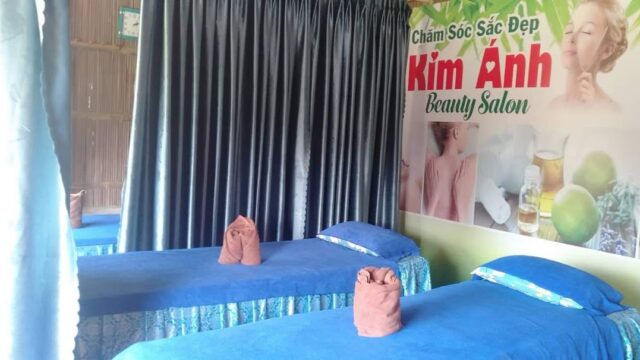 Two spa beds with blue linens, rolled towels, and a Kim Anh Beauty Salon sign in softly lit Hoi An tranquility.