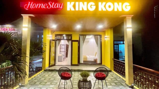 A brightly lit Hoi An homestay entrance with HomeStay KING KONG sign, patio chairs, and a view into a cozy bedroom.