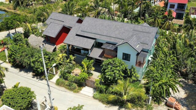 Aerial view of a modern house with a grey roof, set among lush trees on a quiet Hoi An residential street.
