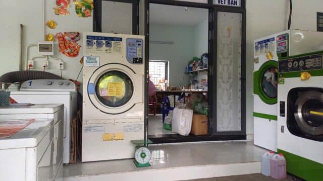 A small laundry shop in Hoi An with washing machines, detergent bottles, and a Laundry Hằng Nga sign above the entrance.
