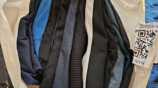 Neatly folded clothes in a bag on a bed in Hoi An, next to part of a blue and yellow blanket and a QR code.