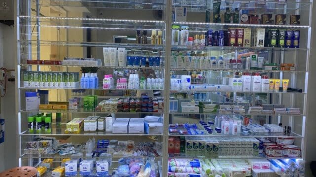 A well-lit pharmacy shelf in Hoi An displays various medicines, skincare, toiletries, and health products organized neatly.