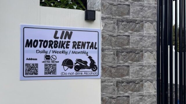 A sign on a stone gate in Hoi An reads LIN Motorbike Rental: Daily, Weekly, Monthly. Do not drink alcohol. QR codes and address included.