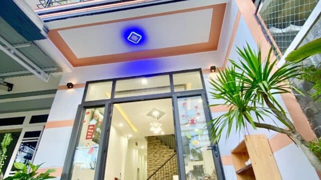 Modern three-story house with large windows, balconies, and lush green plants at the entrance, inspired by Hoi An charm.