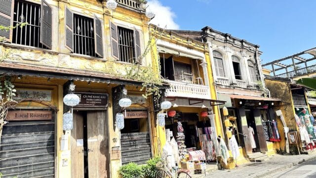 Yellow colonial-style buildings with shops, lanterns, and a bicycle line a sunny street in Hoi An, Vietnam.