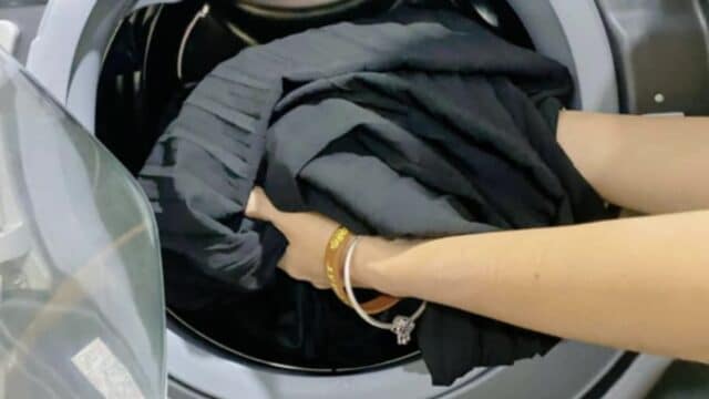 A person in Hoi An loads a black garment into a front-loading washing machine.