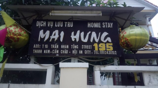 A black Mai Hung Homestay sign with address and phone details in Hoi An, flanked by two yellow lanterns.