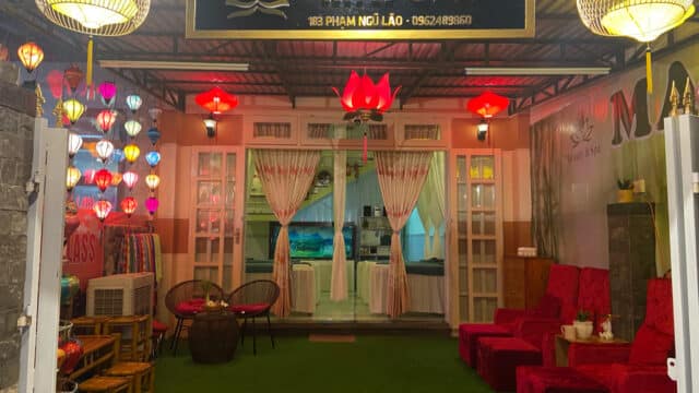 Mai Spa entrance in Hoi An with red lanterns, velvet chairs, round tables, and colorful hanging lights. Sign reads Mai Spa above the door.