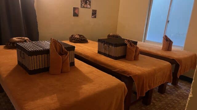 Three massage tables with orange covers, wicker baskets, and towels in a softly lit Hoi An spa room.
