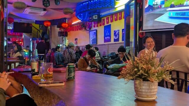 Funky Monkey Bar in Hoi An with patrons watching sports, colorful lights, and Vietnamese flags decorating the lively room.