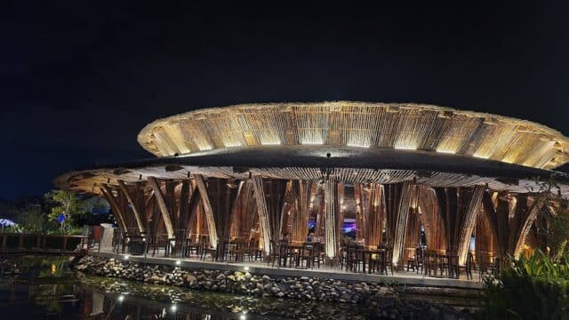 A round, bamboo-structured restaurant in Hoi An is illuminated at night, its lights shimmering in the pond below.